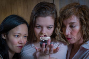 Photo by Ron Diamond of three actors fixing their gazes on a cupcake in I'm Not Here